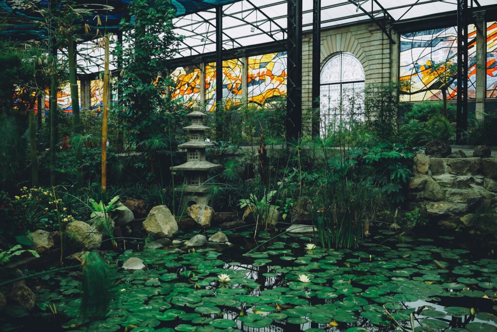 Lush greenhouse interior featuring a serene pond with water lilies and vibrant stained glass windows.